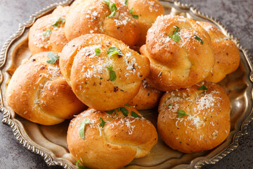 Homemade Buttery Garlic Knot Bread with Parsley and Parmesan cheese and dried greens closeup on the plate on the table. Horizontal
