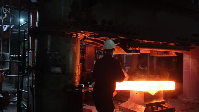Blacksmith factory. Close-up of robots work. Forging a large hot metal billet with an industrial forging press. Technical equipment of a metal forging plant. Large machines, blacksmiths move and heat