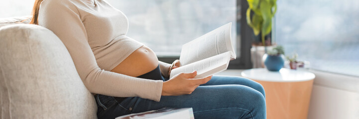 Pregnant woman reading prenatal books preparing for labor, birth, newborn and motherhood sitting on...