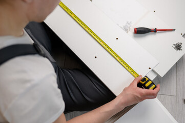 Furniture assembler measures a wooden board with a tape measure, close-up. Construction concept, handyman,furniture assembly