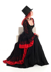 portrait of beautiful red haired woman wearing long black fantasy vampire costume gown, isolated pose on  studio background.