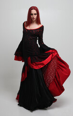 portrait of beautiful red haired woman wearing long black fantasy vampire costume gown, isolated...