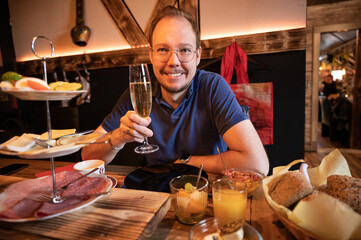 Smiling man drinking a glass of prosecco while sitting at a decorated breakfast table with a...