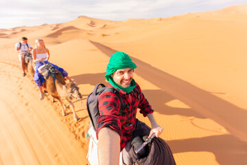 Man enjoying the excursion with group while riding the camel in the desert - obrazy, fototapety, plakaty