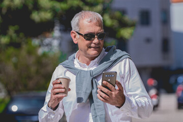 mature man with phone in the street having a coffee - Powered by Adobe