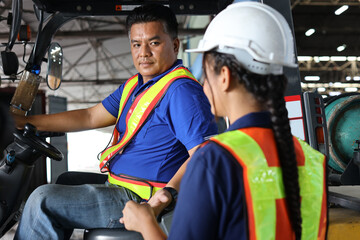 Warehouse worker or forklift driver man with hardhats and reflective jackets in vehicle sending forklift key to colleague woman trainee at inventory in retail warehouse logistics, distribution center