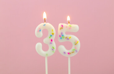 Burning white birthday candles  on pink background, number 35