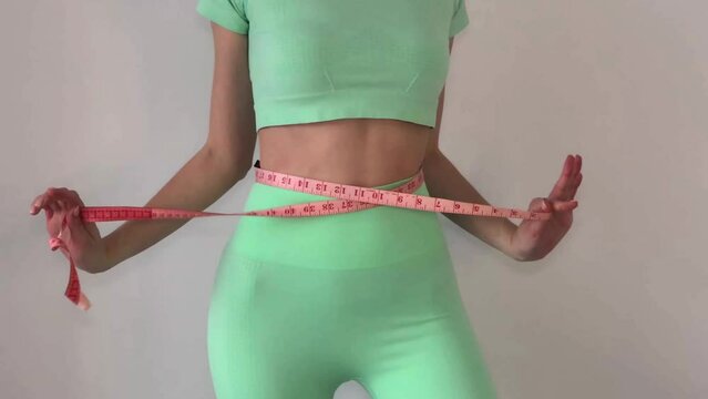 Young slim woman in turquoise spotwear measuring her waist with a tape measure. The concept of diet and weight loss.