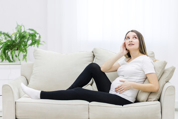 Young pregnant woman thinking about something on white sofa.