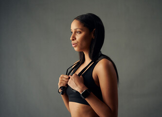 Young biracial woman in sports bra taking a break and exhaling while holding jump rope in studio