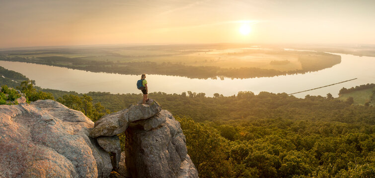 Woman standing on sandstone overhang watching sunrise from summitÂ ofÂ PetitÂ Jean MountainÂ above Arkansas River ValleyÂ 