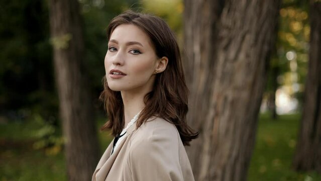 Close-up portrait of beautiful elegant confident smiling young brunette woman in business clothes standing in autumn park.