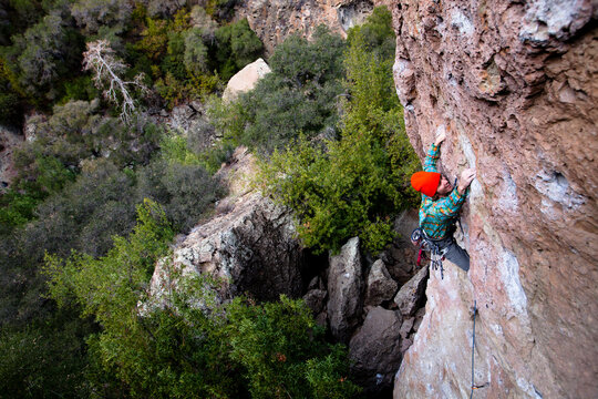 A male climber in an orange beanie and multicolored shirt climbs Family Jewel (5.10d) on Mount Gorgeous in Malibu Canyon State Park in Malibu, California.  Family Jewel is a very p