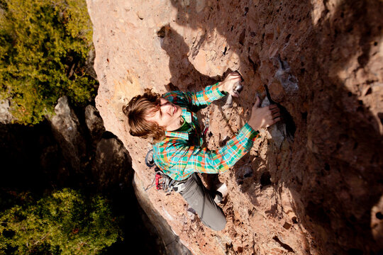 A male climber in an orange beanie and multicolored shirt climbs Family Jewel (5.10d) on Mount Gorgeous in Malibu Canyon State Park in Malibu, California.  Family Jewel is a very p