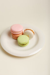 Tasty french macarons on white round plate on light beige background. Cookies for perfect breakfast.