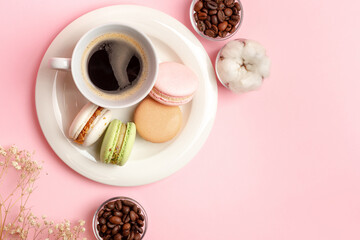 An exquisite french dessert for a perfect breakfast and a cup of coffee. Tasty colored french macarons and cup of hot americano on white round plate, aromatic coffee beans in small glass jar top view