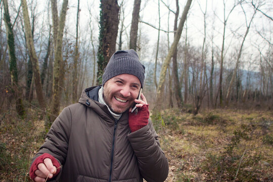The young man is having a cheerful conversation over the phone while walking in the forest.