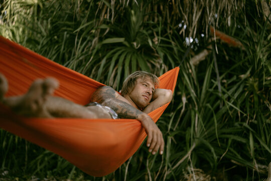 A young man rests and chills in an orange hammock on the beach n