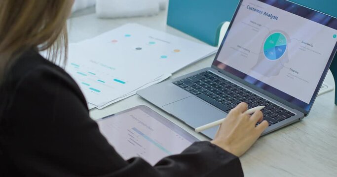 Business woman entrepreneur making data analysis on success plan strategy. Skilled female manage project study paper reports analyze stats infographic on computer screen and tablet pc. Rear back view.
