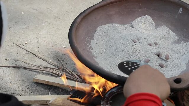 hands of an Asian adult woman, who cooks melinjo fruit using sand heated in a traditional wood stove.