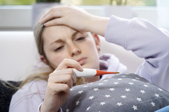 woman is sick and has a fever and reads temperature from a clinical thermometer