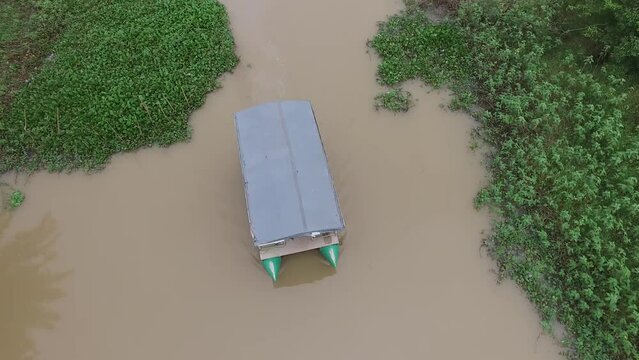 drone camera video, following the movement of a boat sailing over a river with meadows and trees on either side, in Indonesia's Way Kambas Forest National Park.