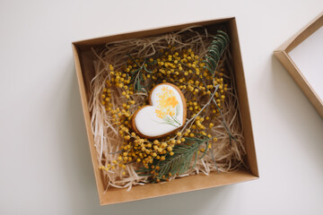 Easter gingerbread cookie in shape of a heart in a gift box with colorful yellow mimosa flowers. Eastet, Spring, April card or banner. Top view