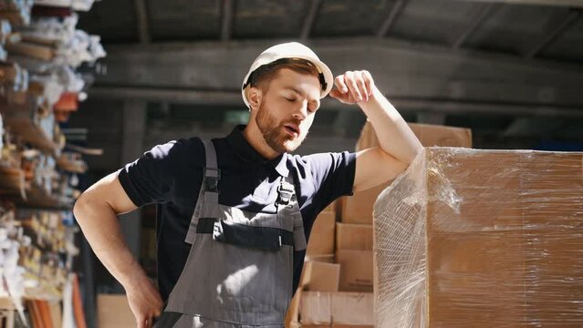 Feeling tired. Taking a break. Storage worker in uniform is in the warehouse.