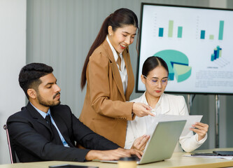Millennial Asian Indian professional multinational male businessmen and female businesswomen in formal business suit standing sitting in meeting room mentoring brainstorming together with laptop