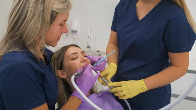 Female dentist with assistant working in dental clinic examining patient teeth.