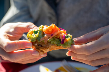Eating salmon avocado sandwich. Woman holds it in hand having lunch outdoors. - 574222875