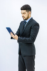 Millennial Asian Indian young professional successful bearded male businessman in formal business suit standing holding using touchscreen tablet computer working online with client on white background