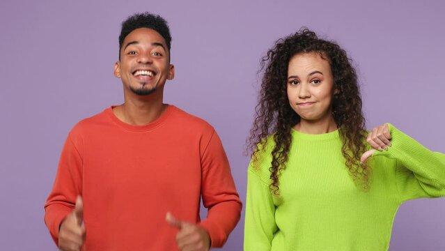 Young couple two friends family man woman of African American ethnicity wear casual clothes together show thumb up thub down disagree isolated on pastel plain light purple background studio portrait