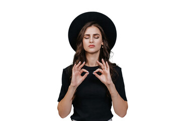 Confident brunette young woman in black hat with brim and black t-shirt eyes closed makes mudra...