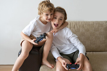 Excited children playing video games PS5 XBOX controller console two kids friends expressing...