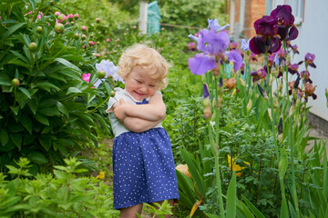 little girl laughing in flowers,a happy child in a garden among flowers of irises and peonies