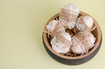 Easter eggs wooden, decorated with lace and braid close-up in a wooden plate on a light yellow background. Copy spaсe. Handmade rustic style