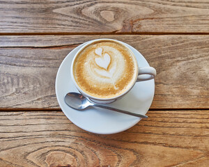 A white cup of cappuccino art coffee with a double heart froth decoration on a raw, veined brown wooden table. Space for your text or logo.