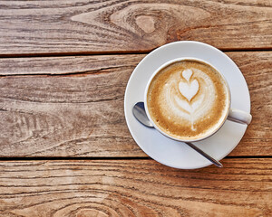 A white cup of cappuccino art coffee with a double heart froth decoration on a raw, veined brown wooden table. Space for your text or logo.