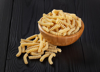 Dry fusilli pasta in wooden bowl on black wooden background