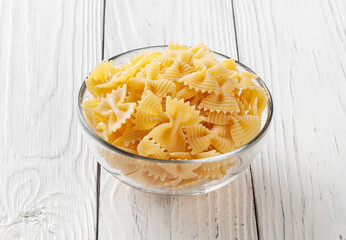 Uncooked farfalle rigate pasta on white wooden background