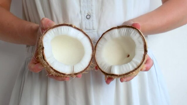 A girl in a white dress divides a coconut into two halves.