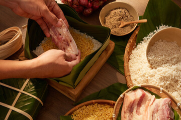 Hands putting fatty pork in box lined with dong leaves when making sticky rice cake (Chung cake)....