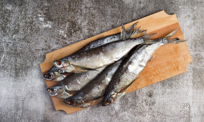 Dry (Air-dried) salted sabrefish or ambassador on a rectangular cutting wooden board on a dark grey background. Top view, flat lay