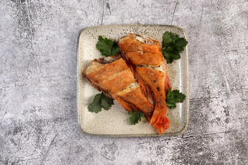 Pan Fried Rose fish with herbs on a square plate on a dark background. Top view, flat lay