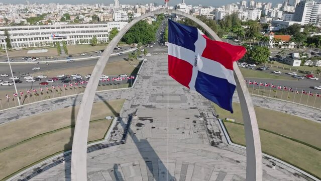 Aerial view of waving flag of Dominican Republic at Plata de la Bandera and Cityscape of Santo Domingo in background  .- Tilt up shot