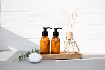 Obraz premium Amber bottles with facial cosmetics on a tray and aroma diffuser with a branch of eucalyptus on the wooden background. Front view