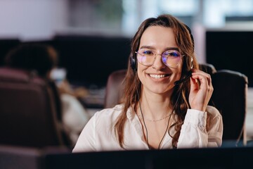 Smiling hotline operator girl consulting clients via headset. Front view of beautiful telemarketer in glasses. Happy young woman working in call center