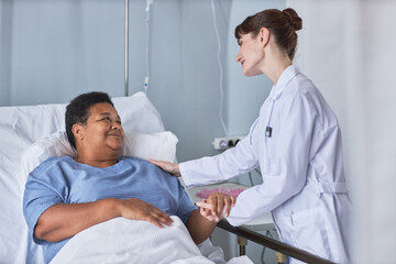 Portrait of African American senior woman on hospital bed with young nurse supporting her