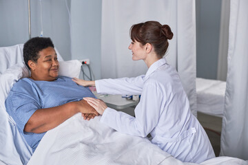 Side view portrait caring young nurse supporting senior female patient in hospital bed